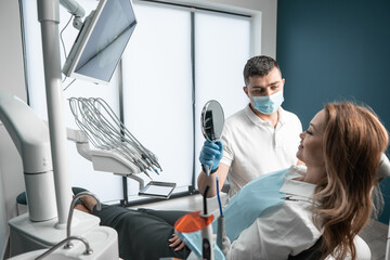 The doctor shows the mirror to the patient to the woman. Procedures at the dental center are...