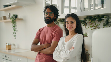 Diverse married couple multiracial homeowners spouses posing arms crossed in domestic kitchen...