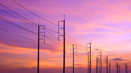 Silhouette row of electric poles with cable lines against colorful sunset sky background, low angle...