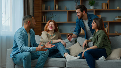 Four ethnic friends fellows companions sit on home couch talking discuss plans chatting friendly talk indoors gathered multiethnic men and women converse joking laughing sharing news real friendship - obrazy, fototapety, plakaty