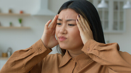 Tired sick Asian woman feel headache pain massaging temples touch aching head hurt grimace suffer...