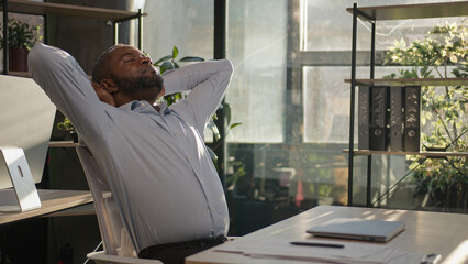 Relaxed African American mature businessman senior happy man finish computer work close laptop relaxing in sunny warm comfortable office male specialist stretch muscles put hands behind head day end - obrazy, fototapety, plakaty