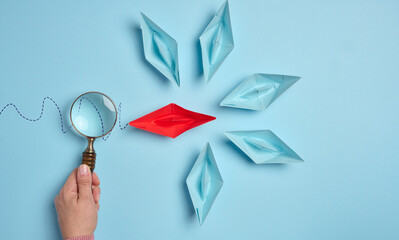 A woman's hand holds a magnifying glass over paper boats, a concept for researching the uniqueness...