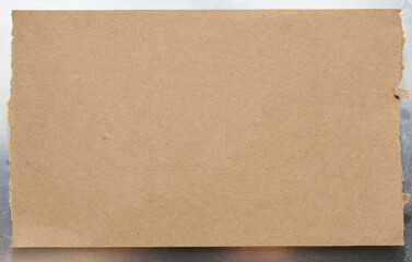 Torn piece of brown cardboard on a gray background