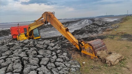 a dirty excavator in the mud lake for arranging the mud to make the dam stronger and higher 