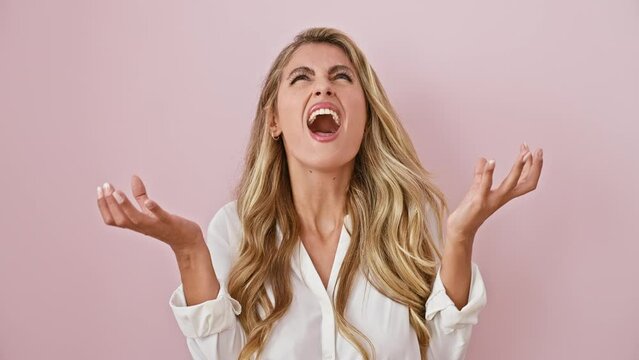 Furious blonde damsel, standing agitated over pink wall, lets out a crazy yell! her arms raised, the mad expression of frustration emerges.