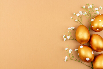 Festive flat lay with golden easter eggs and Gypsophila flowers on brown background wih copy space