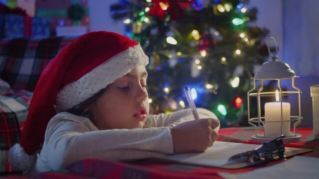Cute girl child writing a letter to Santa Claus at home by the fireplace 
