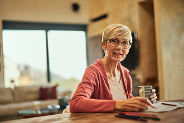 Portrait of a happy senior woman, wearing glasses, looking at the camera, coloring the coloring book.