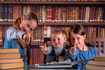 Conceptual image: child development and early learning. Young scientists showing thumbs up sign, studying and reading books  in the library.