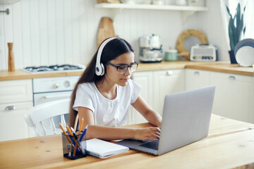 Girl in headphones and eyeglasses e-learning at home - obrazy, fototapety, plakaty