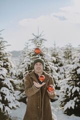 Mann in verschneiter Landschaft jongliert mit roten Christbaumkugeln