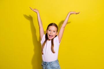 Photo of excited cheerful little child dressed pink t-shirt smiling rising hands arms isolated...
