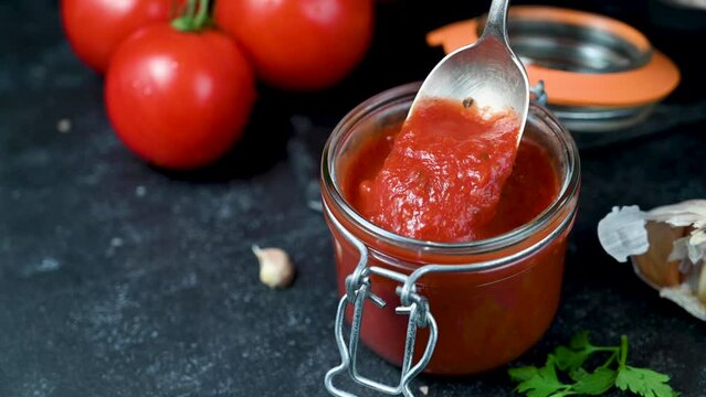 Tomato paste in a glass. Homemade tomatoes sauce, dark background
