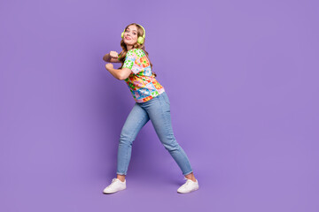 Fototapeta na wymiar Full size photo of lovely positive girl dressed print t-shirt jeans dancing in headphones have fun isolated on violet color background