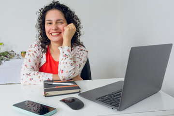 Young entrepreneur latin woman Sitting in her Office leaning on her desk smiling looking at camera