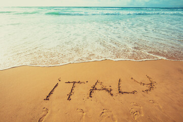 The inscription of Italy on the beach of white sand. Gradient color.
