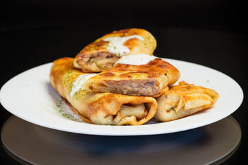 Thin fried pancakes with meat filling in a plate with sour cream and spices.