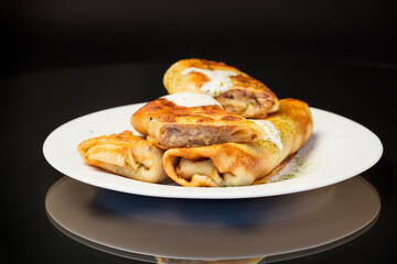 Thin fried pancakes with meat filling in a plate with sour cream and spices.