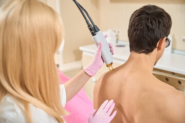 Blonde woman conducts session of laser hair removal on shoulders