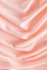 Fototapeta premium Soft pleats of peach colored satin textiles. Luxury abstract textile background design. Vertical view. Color of the Year 2024 peachy fuzz.