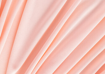 Elegant textile background in peach color with soft pleats. Festive background of the color of the...