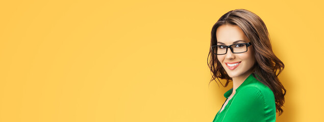Portrait of happy smiling young brunette woman in eye glasses, green smart casual wear, isolated orange yellow background. Business studio concept. Copy space blank area for text. Banner composition