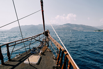 Bow of a wooden sailboat sailing on the sea towards a mountain range