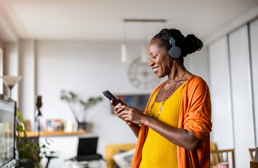 Woman listening to music with headphones connected to her smartphone in the living room at home
