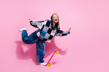 Full size photo of overjoyed eccentric girl dressed jeans pullover riding skateboard to empty space isolated on pink color background