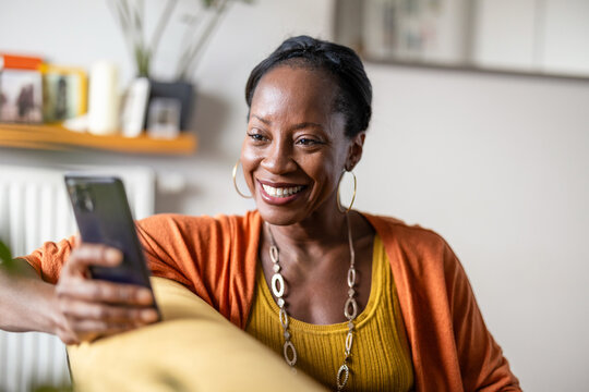 Mature woman using mobile phone while relaxing on sofa at home
