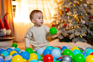 Fototapeta na wymiar A little boy playing with balls in front of a christmas tree. Little Boy's Joyful Playtime in Front of a Festive Christmas Tree