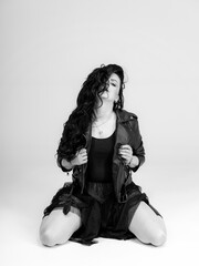 A woman sitting on the ground with a jacket on. A Woman Sitting Outdoors in a Stylish Jacket