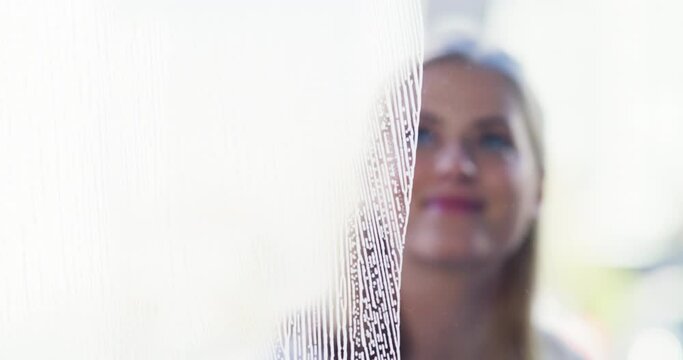 Window, woman and cleaning with a wiper for hygiene, shine and clear vision in home. Face of a young female person with a squeegee, gloves and soap detergent for housework or glass housekeeping