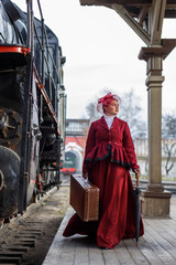 A beautiful girl in a burgundy suit of the last century and a hat with a veil stands with a...
