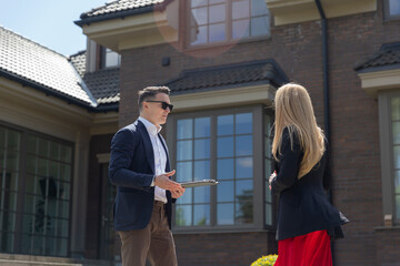 Property agent demonstrates expensive suburban house to woman buyer. Customer observes large villa...