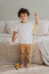 Vertical shoot of curly handsome Spanish boy measuring himself by measuring roulette standing at...