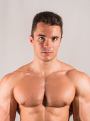 Fototapeta premium Shirtless young male bodybuilder in studio portrait, looking at camera on neutral background, showing muscular torso and body