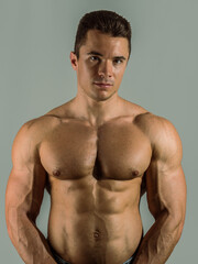 Fototapeta na wymiar Shirtless young male bodybuilder in studio portrait, looking at camera on neutral background, showing muscular torso and body