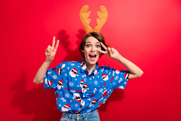 Portrait of cheerful astonished lady show v-sign near eye wear deer x-mas antlers isolated on vivid...