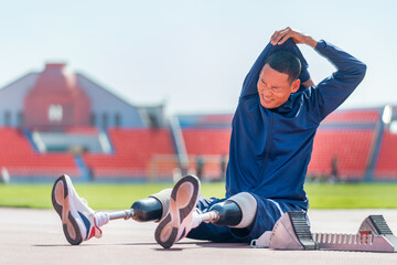 Sport man athlete with a prosthesis on his leg sit on the track and do the stretching of his arm...