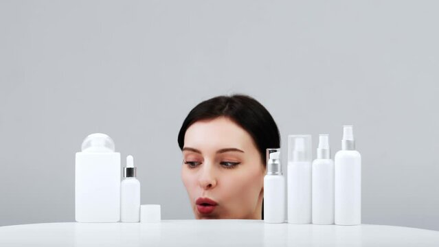 Cosmetics based on natural ingredients, scrub, tonic, body care. Production of natural cosmetics. Young woman on a light background among jars, bottles and tubes for cosmetic procedures on a white bac
