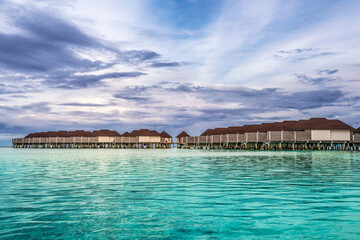 Obraz premium Scenic view of water villas in Maldives after sunset with turquoise pristine water and dramatic sky 