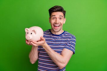 Photo of impressed guy with stubble dressed t-shirt holding piggy box in arms astonished staring...