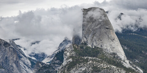 The sheer granite face of Half Dome, shrouded in clouds, on an autumn day in Yosemite National Park in California.