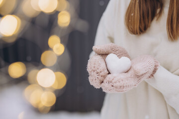 Female hands in knitted mittens hold snow heart on gray winter background