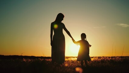 Mama walks with daughter telling childhood secrets under light of sunset in park. Young mama gives...