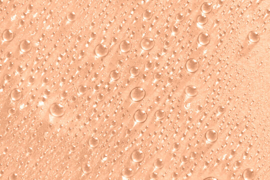 Abstract cosmetic background of a drop of moisturizing liquid on a peach background. Moisturizer tonic, lotion, serum. Beautiful trendy peach fuzz color background.