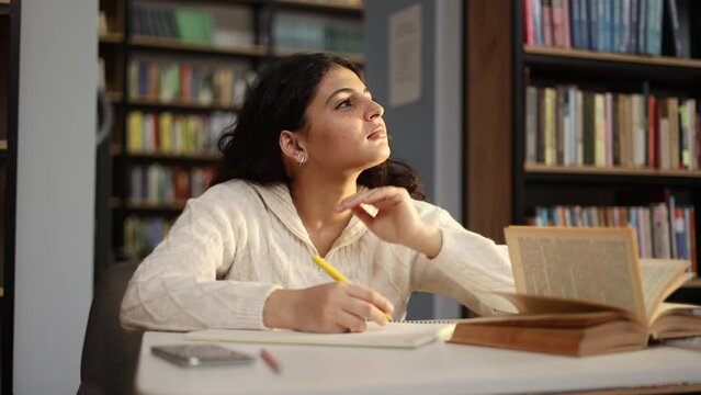 Pretty doubtful creative young woman student searching inspiration thinks questioningly about difficult choice choose imagine plan in mind has doubts create idea at desk at university library