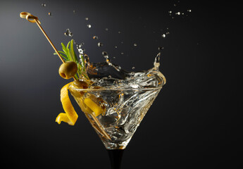 Classic dry martini cocktail with green olives, lemon peel, and rosemary on a black background.